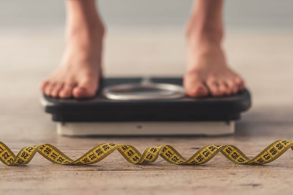 A person standing on a scale and a tape measure in front of the scale